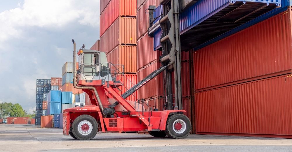 A red reach stacker moves a shipping container.