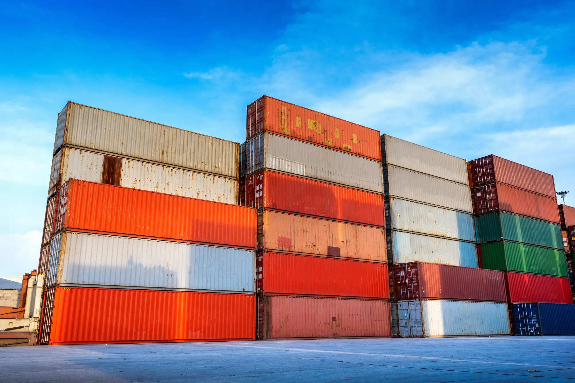 Stacked multicolored shipping containers in an outdoor freight yard under a bright blue sky