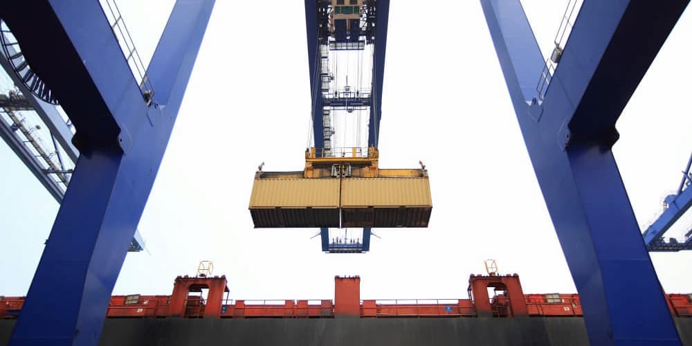 A shipping container is hoisted by a large blue crane above a cargo ship, highlighting maritime trade.