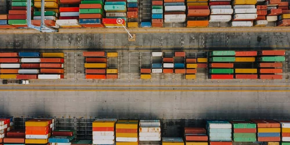 Aerial view of a busy shipping port with rows of colorful stacked shipping containers in various sizes, creating a vibrant, organized pattern.
