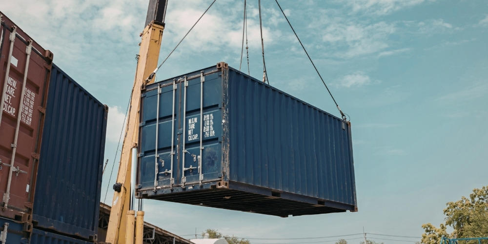 yellow mobile crane hoisting a large dark blue shipping container